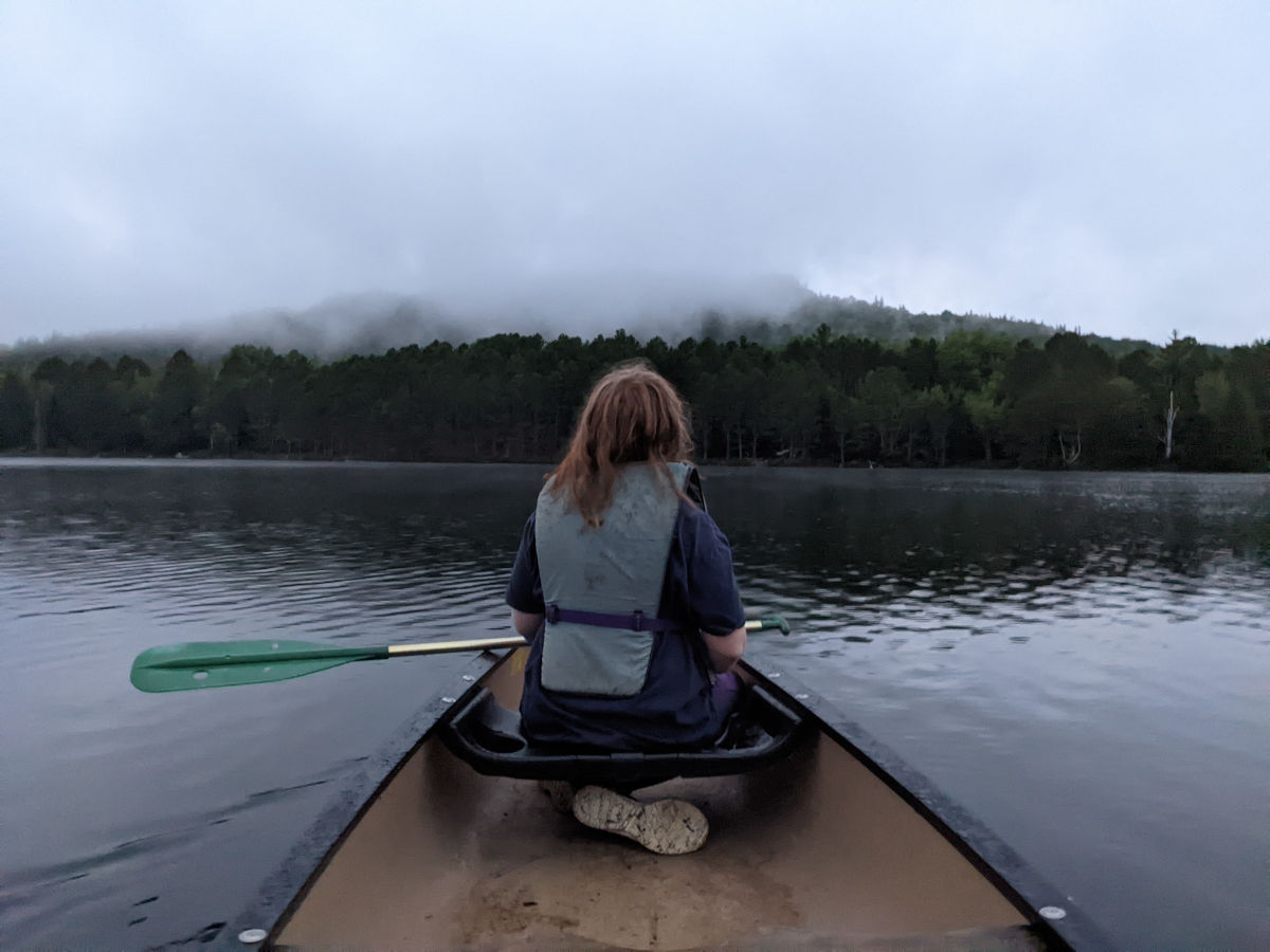 Fiona in the bow seat taking a break from paddling to look at the fog around the mountain