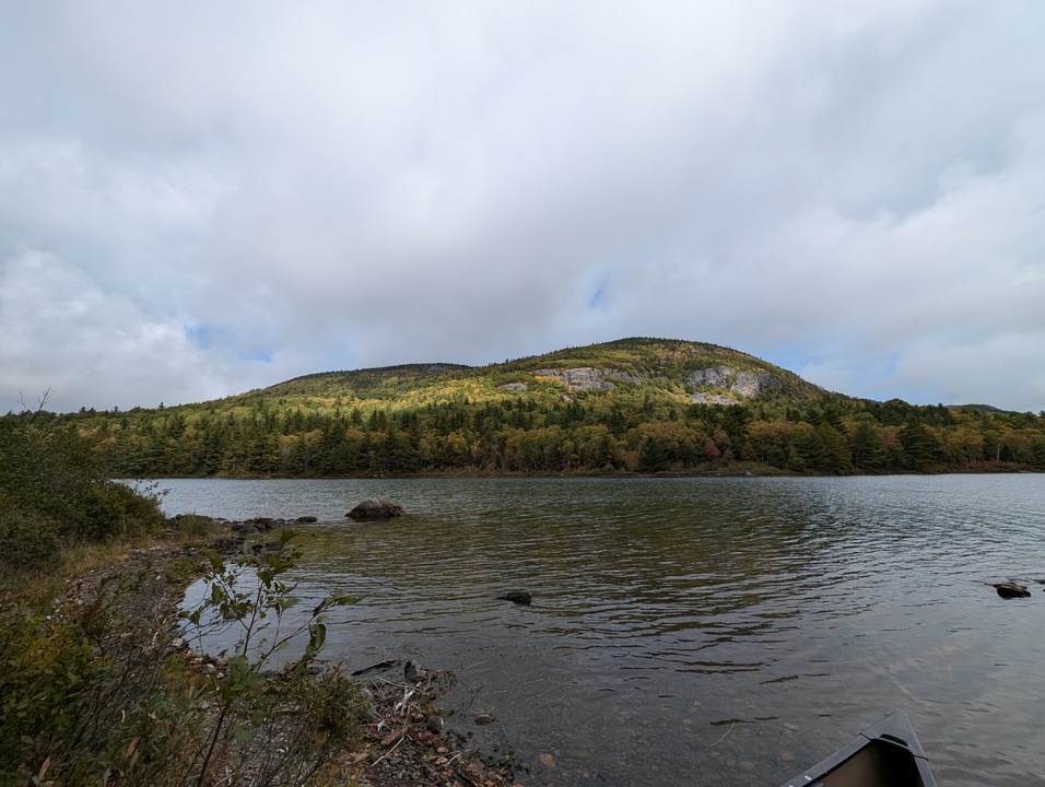 Mountain with sunny and cloudy spots and canoe on lake