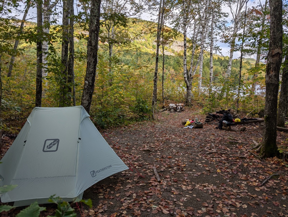 Camp site with tent, fire pit, and gear and lake and Billfish mountain in background