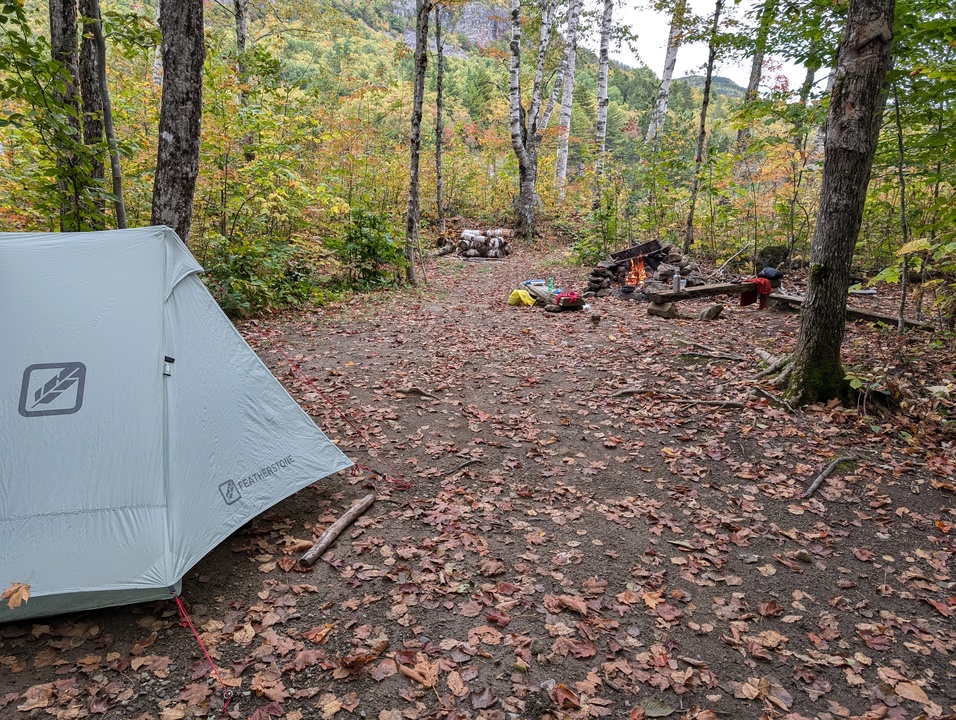 Camp site with tent in foreground, gear in background, fire in fire pit