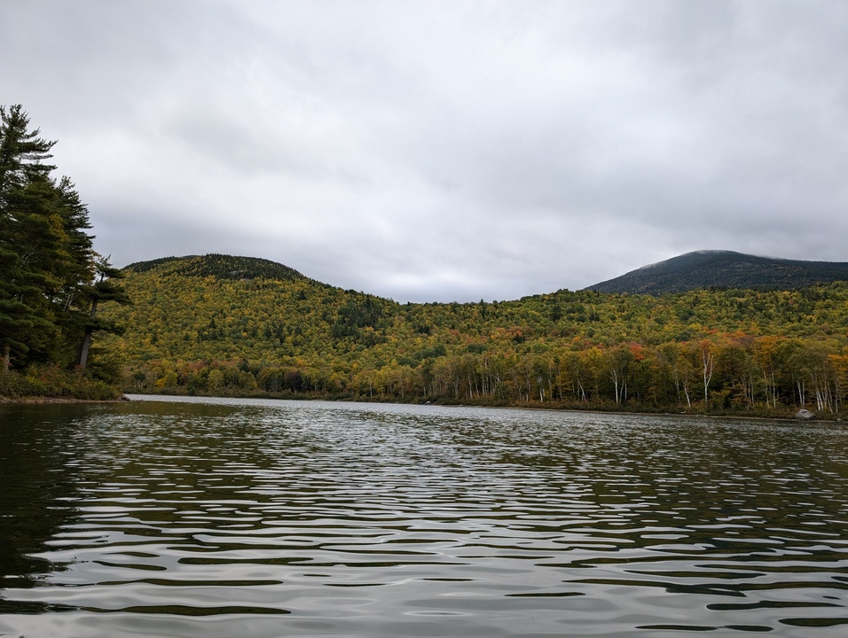 Two mountains, one partially obscured by cloud with fall colored trees