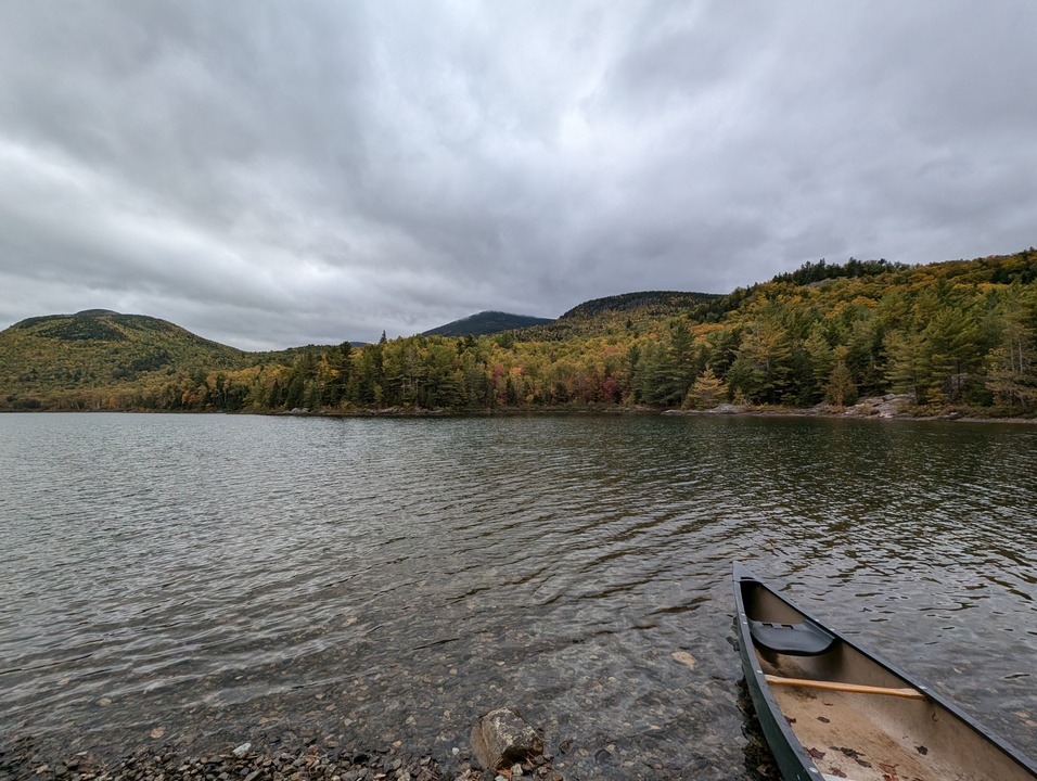 Slightly ripply lake with canoe in foreground and three mountains in the background