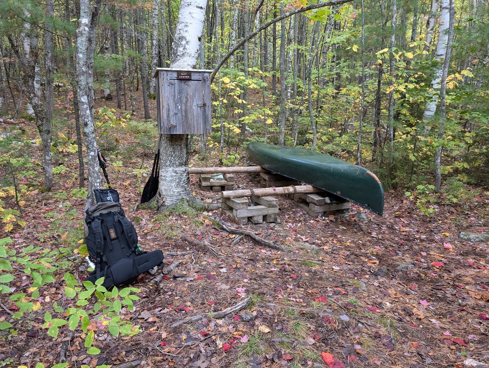 Backpack leaning against a tree next to canoe on a rack