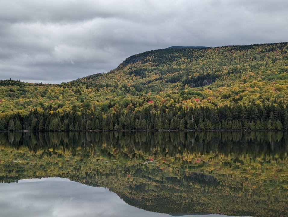 Mountainside reflected in lake with fall colored trees with another mountain in background